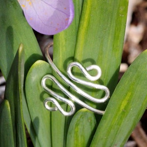 May include: A silver wire ring with a unique, abstract design. The ring is made of multiple loops and curves, creating a modern and stylish look.