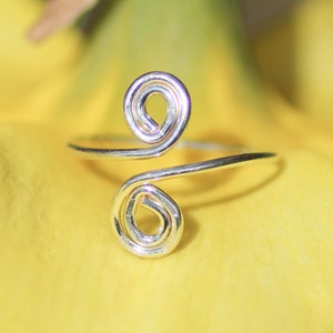 May include: A silver ring with two intertwined spirals. The ring is made of wire and has a simple, elegant design.