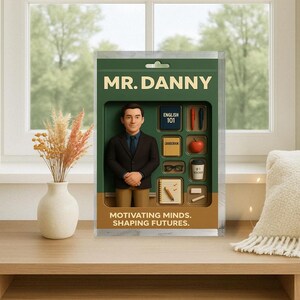 以下が含まれることがあります： スーツ姿の男性のフィギュアで、「Mr. Danny」とラベル付けされ、ミニチュアの学校をテーマにしたアイテムが付属しています。「Motivating Minds. Shaping Futures.」と書かれたパッケージ。小さなリンゴ、メガネ、コーヒーカップが含まれています。