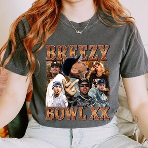 A person wearing a gray t-shirt with a graphic design featuring a group of baseball players and the text "BREZZY BOWLXX".