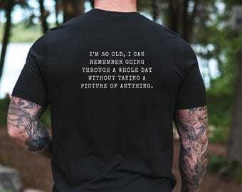 Op de afbeelding: Een zwart t-shirt met korte mouwen en witte tekst op de achterkant die luidt: I'M SO OLD, I CAN REMEMBER GOING THROUGH A WHOLE DAY WITHOUT TAKING A PICTURE OF ANYTHING. Het t-shirt heeft een ronde hals en een standaard pasvorm.