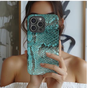 Op de afbeelding: Een telefoonhoesje met een teal en zwart slangenpatroon. De hoes heeft een glanzende afwerking en een camera-uitsparing met drie lenzen. De telefoonhoes wordt voor het gezicht van een persoon gehouden.