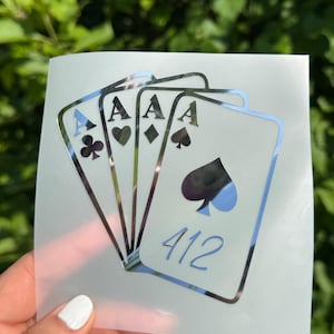 May include: A silver metallic decal featuring a fan of four playing cards, each displaying the letter A and a different suit symbol. The front card prominently features a large spade symbol and the number 412 printed in a blue script font.