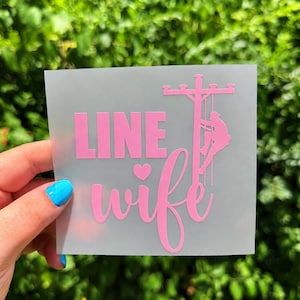 May include: A square, semi-transparent decal featuring the light pink text "LINE" in a bold, sans-serif font above the word "wife" in a cursive script, with a small heart icon and a silhouette of a utility worker climbing a power pole.