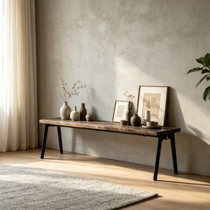 Puede incluir: Banco de madera rústico con patas de metal negro, exhibiendo varios jarrones de cerámica, cuencos pequeños y obras de arte enmarcadas. El banco está colocado contra una pared de tonos neutros, con una alfombra suave y cortinas transparentes.