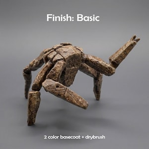 May include: A brown, textured, multi-legged creature figurine with a stone-like appearance. The text "Finish: Basic" appears at the top, and "2 color basecoat + drybrush" is printed at the bottom. The figure has segmented limbs and a shell.