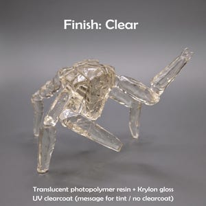 May include: A clear, translucent photopolymer resin figurine shaped like a multi-legged creature with a faceted, geometric surface. The text "Finish: Clear" and "Translucent photopolymer resin + Krylon gloss UV clearcoat (message for tint / no clearcoat)" is visible.