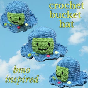 May include: A blue crochet bucket hat with a green square face and a smiling mouth. The hat has a ruffled brim and is decorated with colorful dots. The text "bmo inspired" is written below the hat.