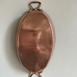 May include: A copper oval baking dish with two handles. The dish has a shiny, polished finish.