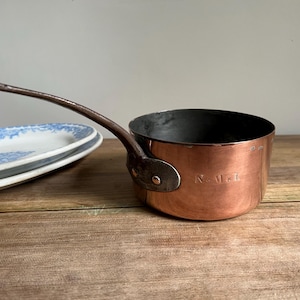 May include: A copper saucepan with a long handle and a black interior. The saucepan has a small, round, metal knob on the handle and the words "New York" engraved on the side.