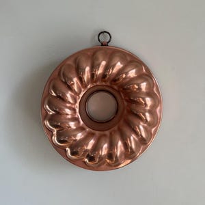May include: A copper bundt cake pan with a fluted design. The pan has a ring handle and is ready to be used for baking.