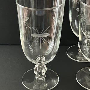 Op de afbeelding: Heldere wijnglazen met geëtste bloemmotieven. De glazen hebben een afgeronde kom, een decoratieve steel en een cirkelvormige voet. Het geëtste ontwerp toont een centrale bloem met stralende lijnen en kleinere bloemaccenten.