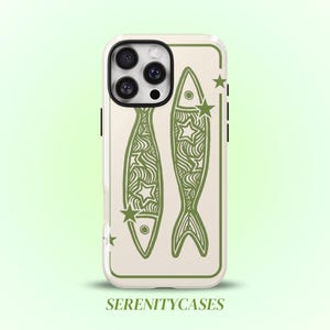 May include: A phone case with a cream-colored background featuring two olive green fish illustrations decorated with wavy lines and star shapes. The design is enclosed in a thin olive green rectangular border. The text SERENITYCASES appears below.