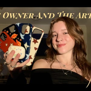 May include: A collection of three smartphone cases featuring star patterns in red, navy blue, and cream, alongside a white wireless earbud charging case with colorful star and heart graphics. The text THE OWNER AND THE ARTIST appears above.