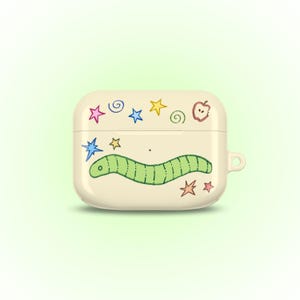 May include: Off-white AirPod case with a whimsical design. The case features a green worm, colorful stars, and an apple illustration. The case has a small loop for attaching to a keychain or lanyard. The design is playful and cartoonish.