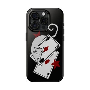 May include: Black phone case featuring a white cat design with playing cards and red star accents. The cat is perched above two playing cards, with a red star on the top and bottom. The case has a glossy finish.