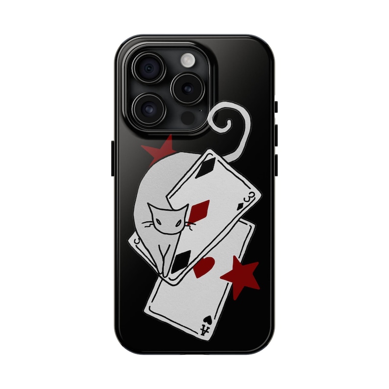 May include: Black phone case featuring a white cat design with playing cards and red star accents. The cat is perched above two playing cards, with a red star on the top and bottom. The case has a glossy finish.