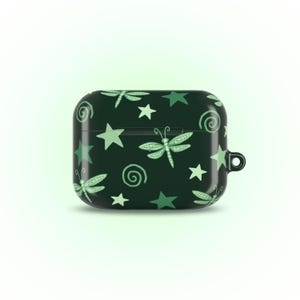 May include: A dark green AirPod case featuring a pattern of light green dragonflies, stars, and spiral designs. The case has a small loop for attaching to a keychain or lanyard. The overall design is whimsical and nature-inspired.