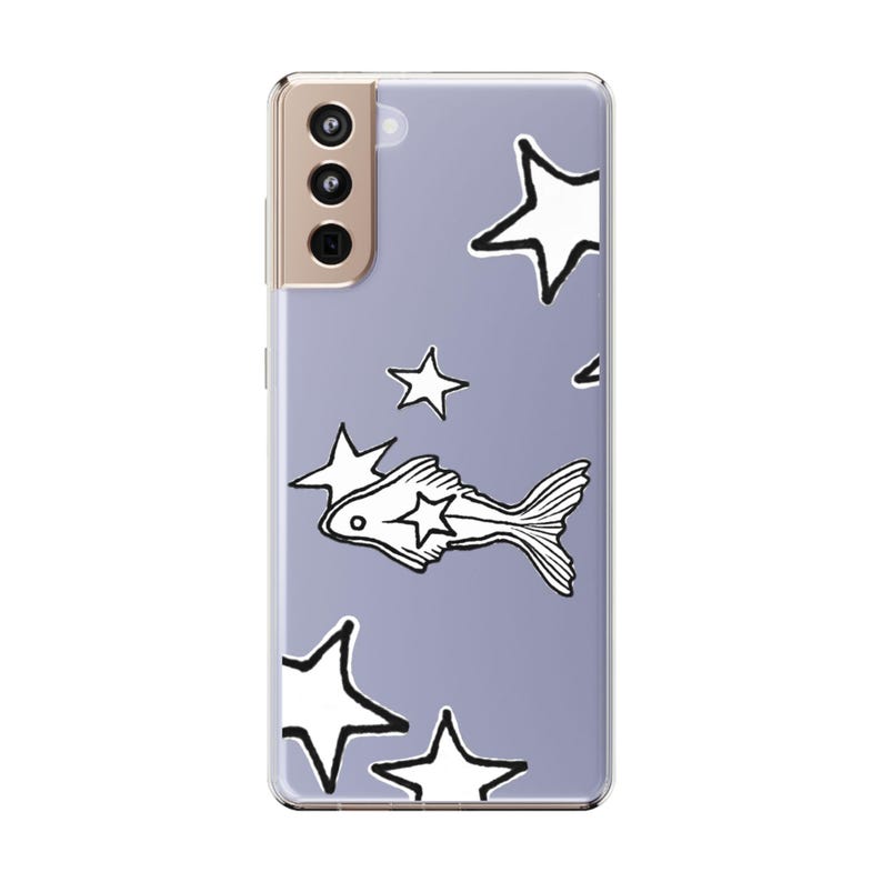 Puede incluir: Funda transparente para tel&eacute;fono con fondo lavanda que presenta un patr&oacute;n de estrellas blancas y una ilustraci&oacute;n de pez. La funda del tel&eacute;fono tiene un m&oacute;dulo de c&aacute;mara y botones dorados.