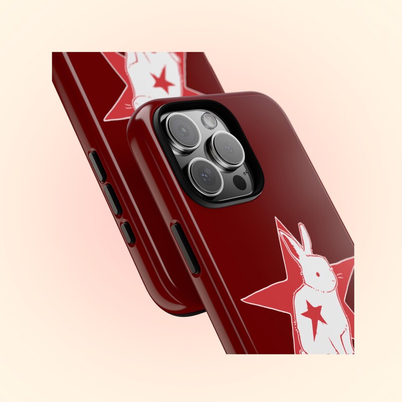 May include: Two crimson phone cases with a glossy finish. Each case features a white rabbit illustration inside a red star. The cases are angled, showcasing the camera and side buttons.