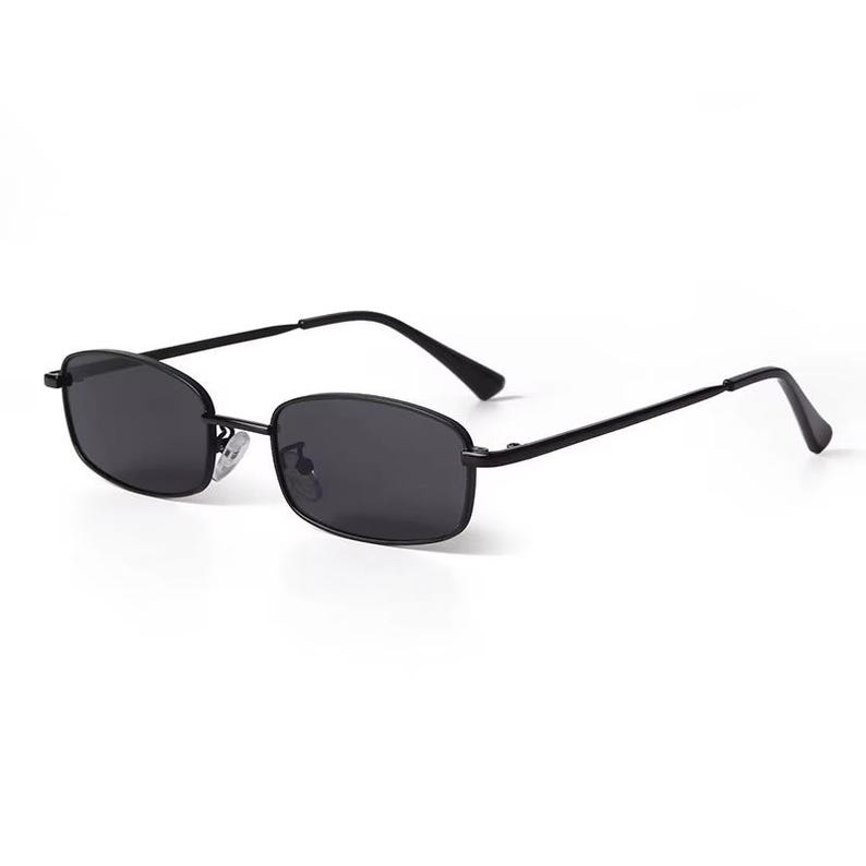 May include: Black rectangular sunglasses with dark lenses and a thin black metal frame. The sunglasses have a classic, minimalist design, suitable for various styles. The lenses appear to be tinted, offering protection from the sun.