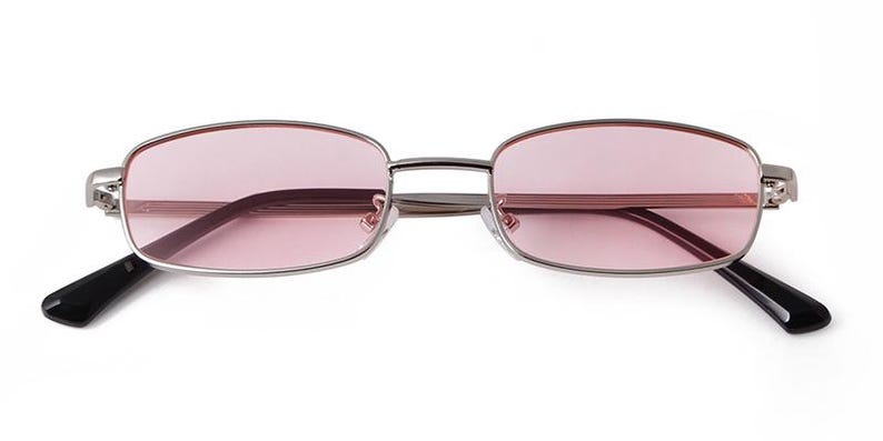 May include: Rectangular-framed sunglasses with a silver metal frame and pink lenses. The temples are black. The glasses are displayed on a white background.