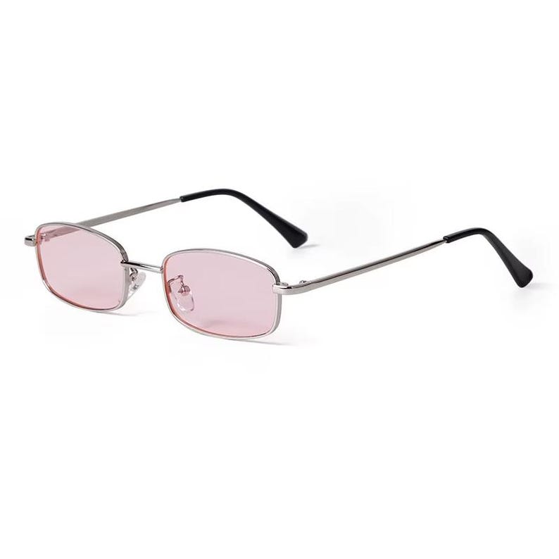 May include: Rectangular sunglasses with a silver frame and pink lenses. The temples are silver with black tips. These stylish sunglasses offer a retro aesthetic.