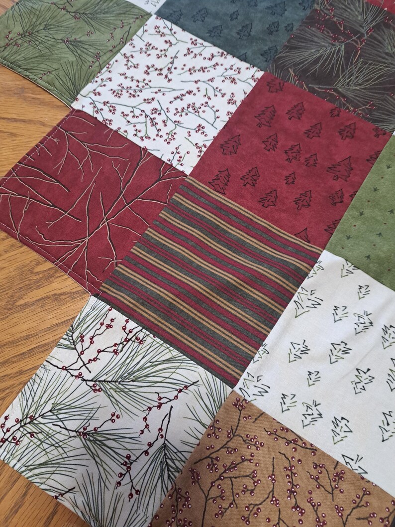 Pu&ograve; includere: Una trapunta patchwork a tema natalizio. I quadrati presentano motivi di aghi di pino, bacche, alberi e strisce nei toni del rosso, verde, marrone e bianco. La trapunta &egrave; probabilmente fatta a mano e adatta per le decorazioni stagionali.