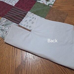 Pu&ograve; includere: Una trapunta patchwork con quadrati di vari motivi e colori, tra cui rosso, verde e bianco. La trapunta ha un retro bianco con la scritta "Back" stampata sopra. La trapunta &egrave; su una superficie di legno.