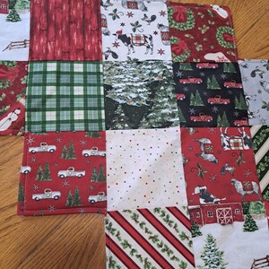 May include: A patchwork Christmas fabric with diverse patterns. The squares display red trucks, snowy scenes, plaid, and festive designs. The colour palette includes red, green, white, and grey.