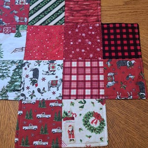 May include: A patchwork Christmas table runner with festive patterns. Squares show trucks, sheep, trees, and Santa Claus. Colours include red, green, white, and black. The runner is made of fabric and has a stitched border.