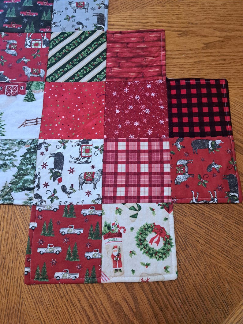 May include: A patchwork Christmas table runner with festive patterns. Squares show trucks, sheep, trees, and Santa Claus. Colours include red, green, white, and black. The runner is made of fabric and has a stitched border.