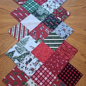 May include: A patchwork Christmas table runner with a diamond pattern. The runner displays festive designs such as red trucks, Christmas trees, plaid, and holiday-themed prints. The colour scheme includes red, green, white, and black.
