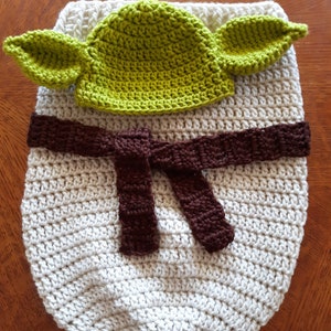 May include: A crocheted baby sleeping bag in white with a brown belt and a green crocheted hat with ears.