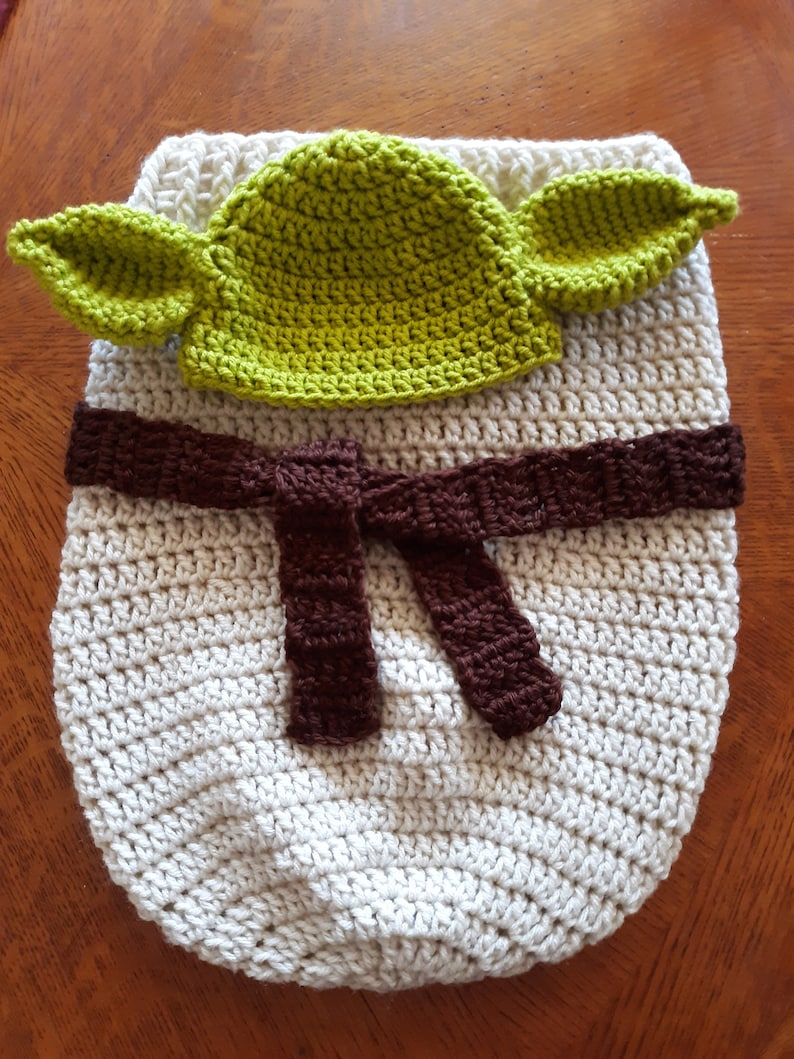 May include: A crocheted baby sleeping bag in white with a brown belt and a green crocheted hat with ears.