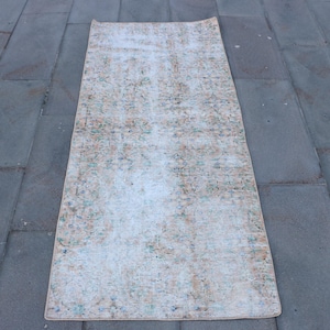 May include: A rectangular runner rug featuring a faded, distressed pattern in muted shades of peach, light blue, and cream. The textile displays an intricate, worn-out floral and geometric motif across its entire surface, with frayed edges.
