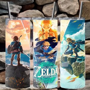 May include: Three stainless steel tumblers with different designs featuring characters from the video game "The Legend of Zelda: Tears of the Kingdom". The tumblers are on a background of stacked rocks.