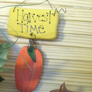 May include: A yellow sign with the text "Harvest Time" hanging from a wire. A small orange pumpkin and a brown candle are in the background.