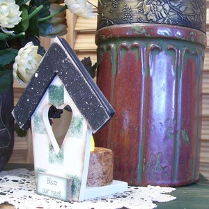 May include: A white birdhouse with a black roof and green and white checkered accents. The birdhouse has a heart-shaped opening and a sign that reads "Bless our nest".