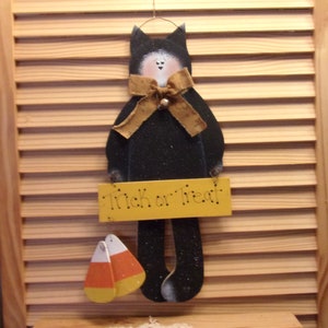 May include: Black cat Halloween decoration with a yellow "Trick or Treat" sign, a brown bow, and candy corn accents.