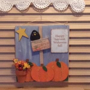 May include: A wooden sign with a blue background and a welcome to the pumpkin patch sign. The sign also has a black bird, a yellow star, and a sign that says "Happy harvest welcome fall".