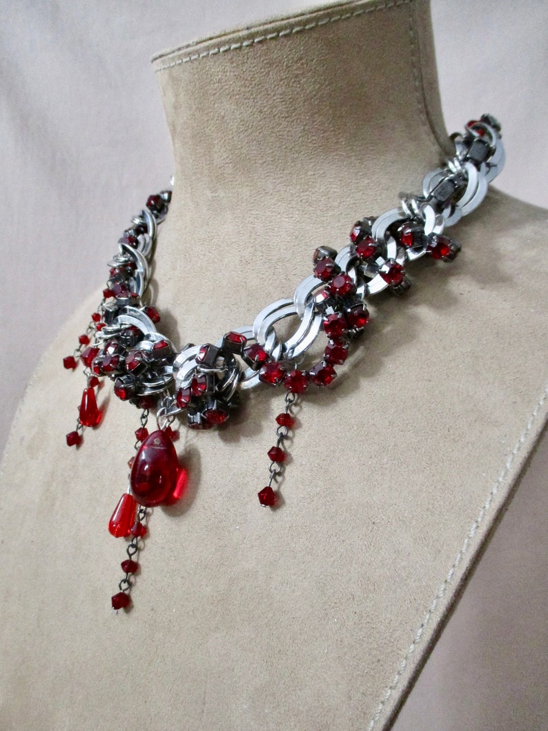 Puede incluir: Un collar de cadena plateada con detalles de cristal rojo y cristales de l&aacute;grima rojos colgantes.