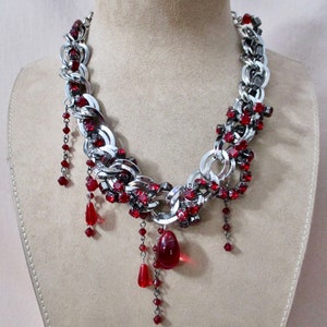 Puede incluir: Un collar de cadena plateada con detalles de cristal rojo y un gran colgante de cristal rojo. El collar est&aacute; en un maniqu&iacute;.