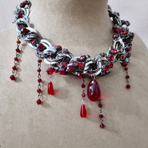 Puede incluir: Un collar de cadena de plata con detalles de cristal rojo y cuentas de l&aacute;grima roja colgantes.