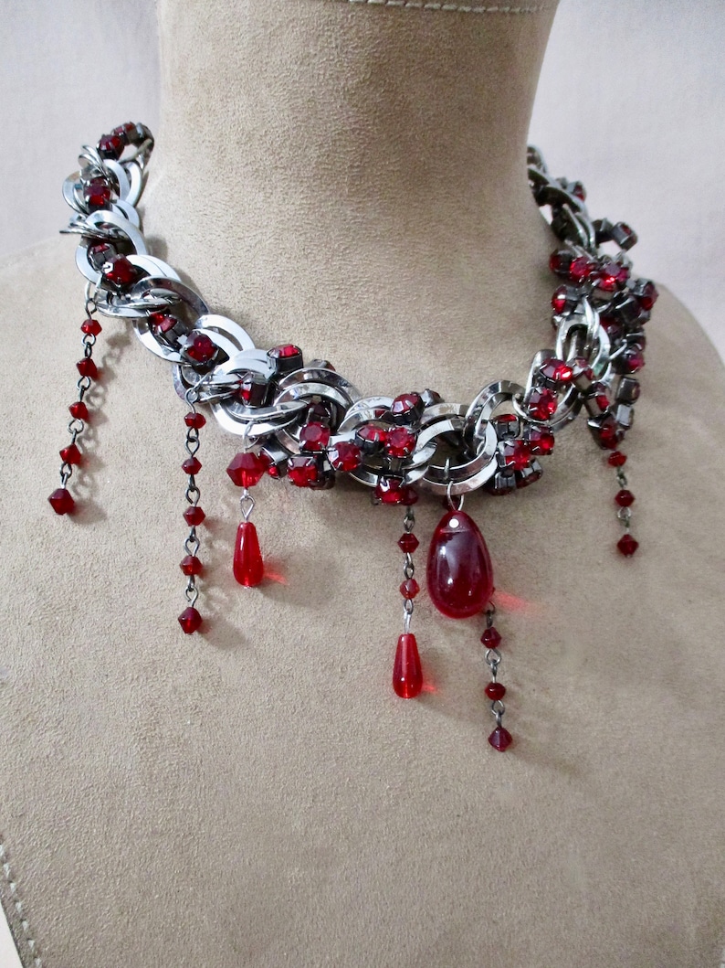 Puede incluir: Un collar de cadena de plata con detalles de cristal rojo y cuentas de l&aacute;grima roja colgantes.