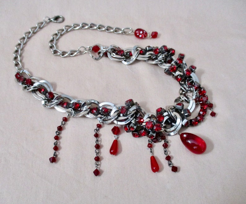 Puede incluir: Un collar de cadena de plata con acentos de pedrer&iacute;a roja. El collar tiene un dise&ntilde;o colgante con m&uacute;ltiples hebras de cuentas rojas.