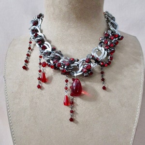 Puede incluir: Un collar de cadena de plata con detalles de cristal rojo y gotas de cristal rojo colgantes.