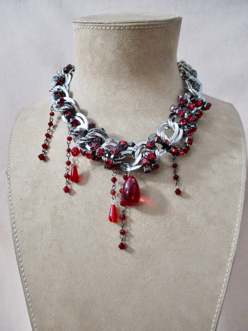 Puede incluir: Un collar de cadena de plata con detalles de cristal rojo y gotas de cristal rojo colgantes.
