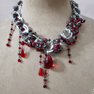 Puede incluir: Un collar de cadena de plata con detalles de cristal rojo y gotas de cristal rojo colgantes.