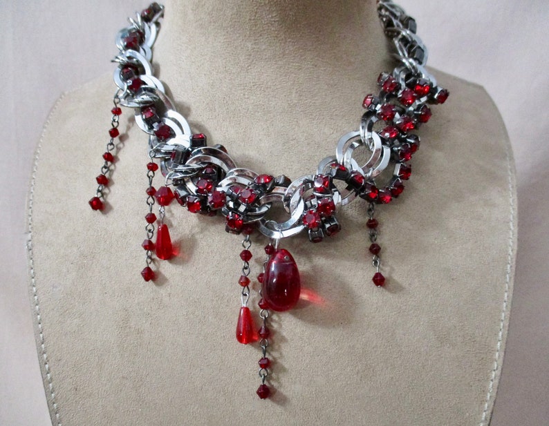 Puede incluir: Un collar de cadena de plata con detalles de cristal rojo y gotas de cristal rojo colgantes.